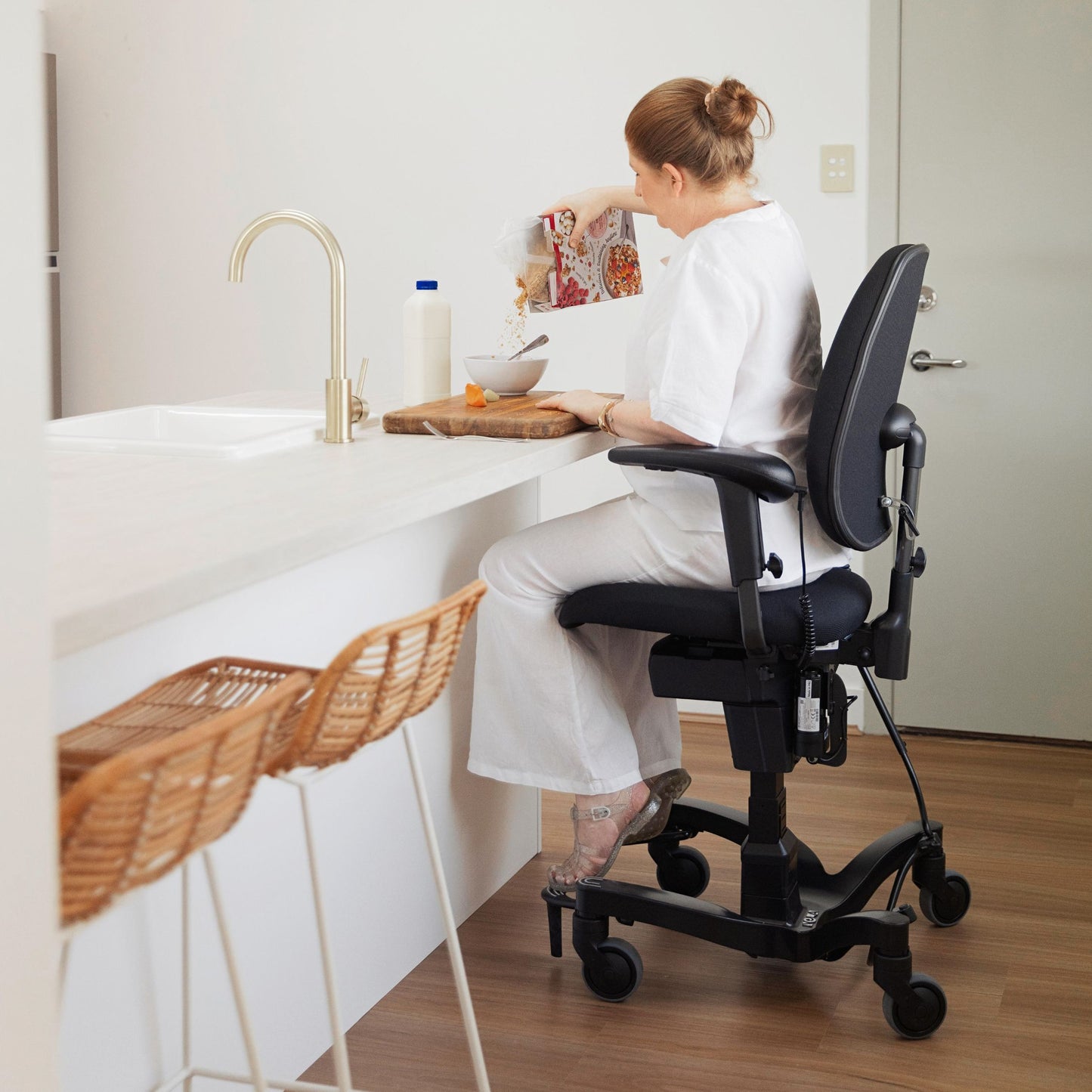 Person sitting at the kitchen bench at height in a VELA Activity Chair making breakfast