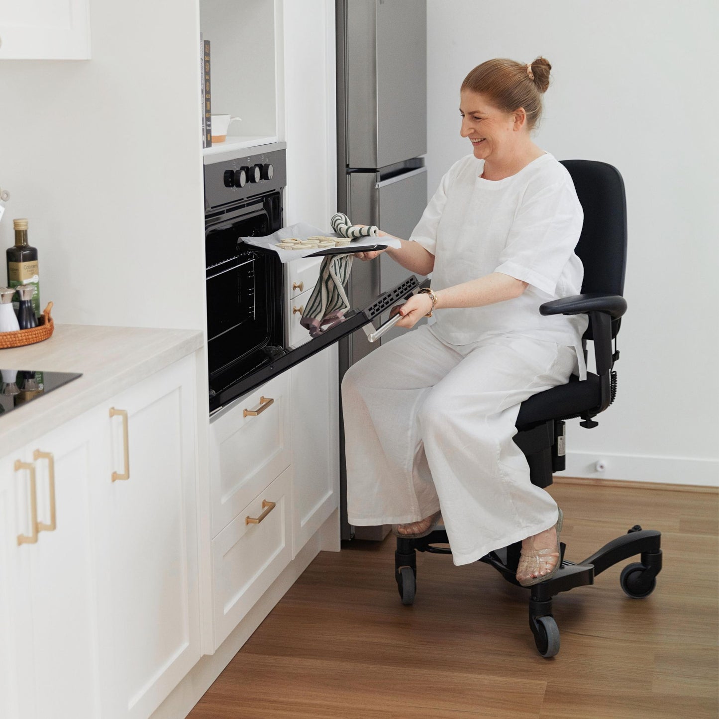 Person putting a tray of quiche into the oven while sitting on a VELA Activity Chair