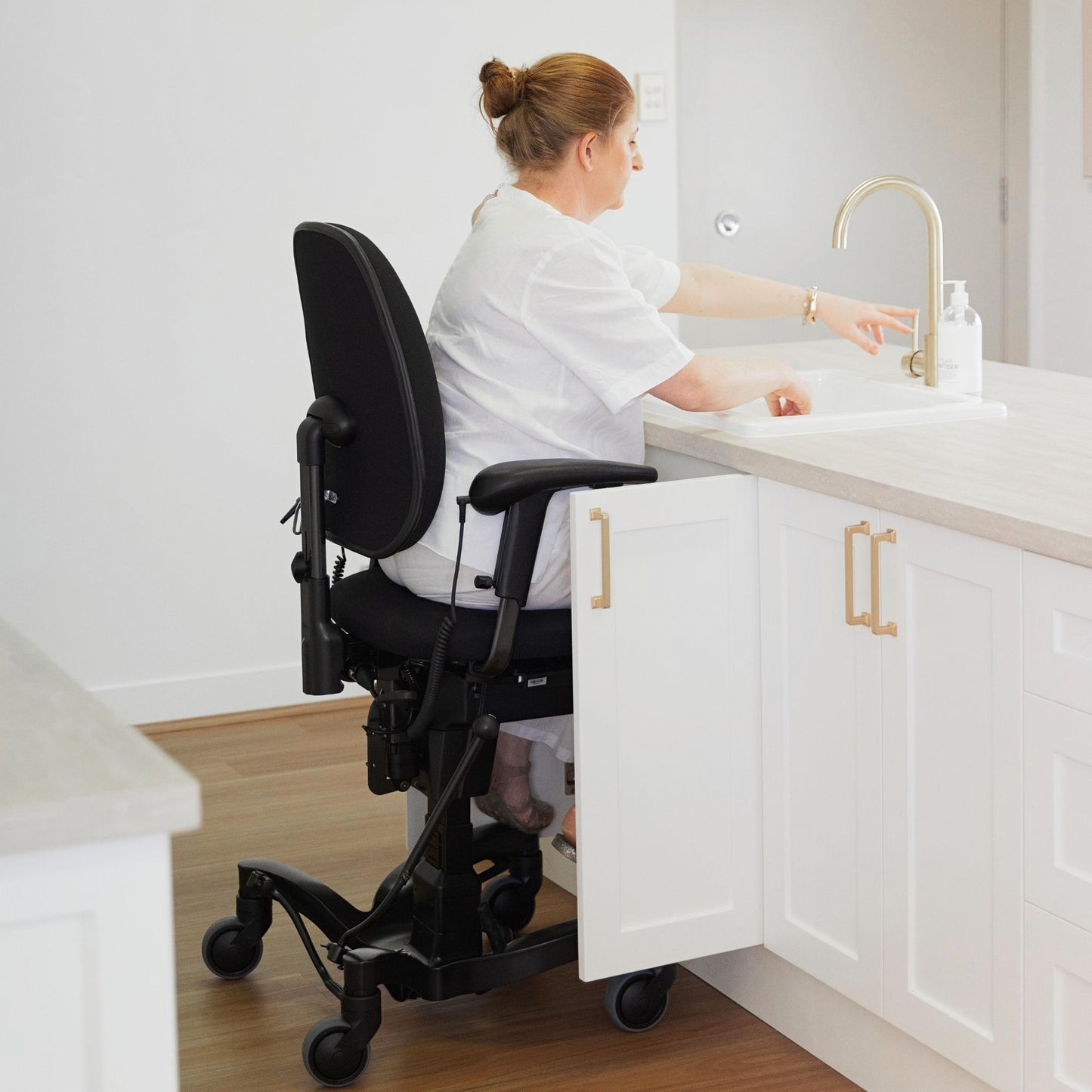 Person in the kitchen washing their hands reaching to the tap while sitting in a VELA Activity Chair
